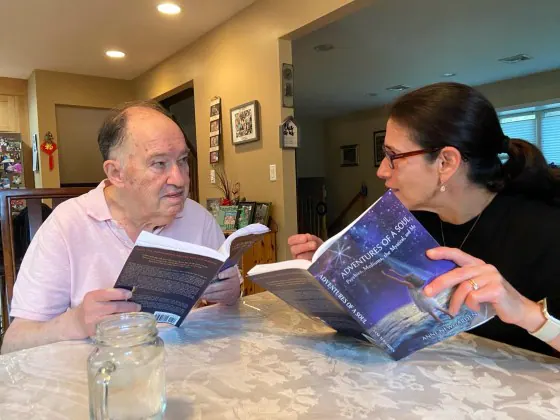 A woman and an older man reading Adventures of a Soul at a table