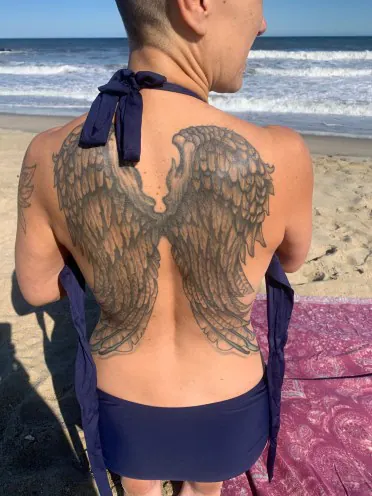 A person at the beach with angel wings tattooed across their back