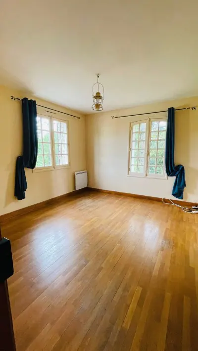 An empty room with wood floors and two windows in the family home