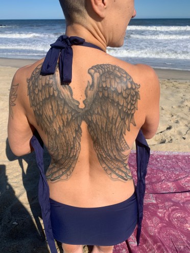 A person at the beach with angel wings tattooed across their back