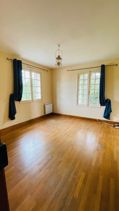 An empty room with wood floors and two windows in the family home