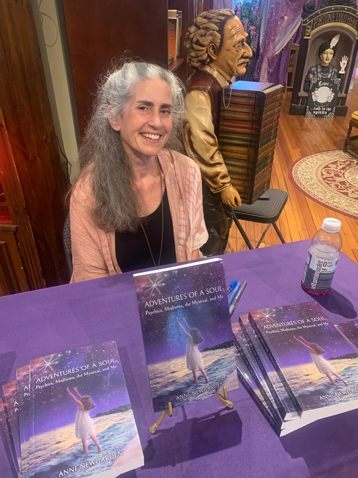 Anne Newgarden seated behind a table of Adventures of a Soul books at LightClub Curiosity Shoppe